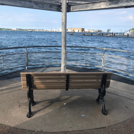 A picture of a wooden and metal chair overlooking Lake Ontario from the harbour.