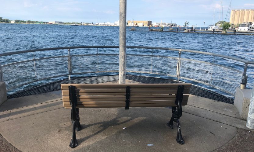 A picture of a wooden and metal chair overlooking Lake Ontario from the harbour.