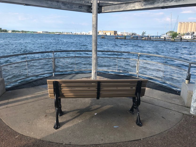 A picture of a wooden and metal chair overlooking Lake Ontario from the harbour.